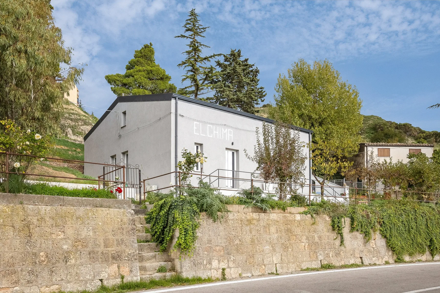 Shared amenity: A white building stands above a stone retaining wall amid trees and greenery.