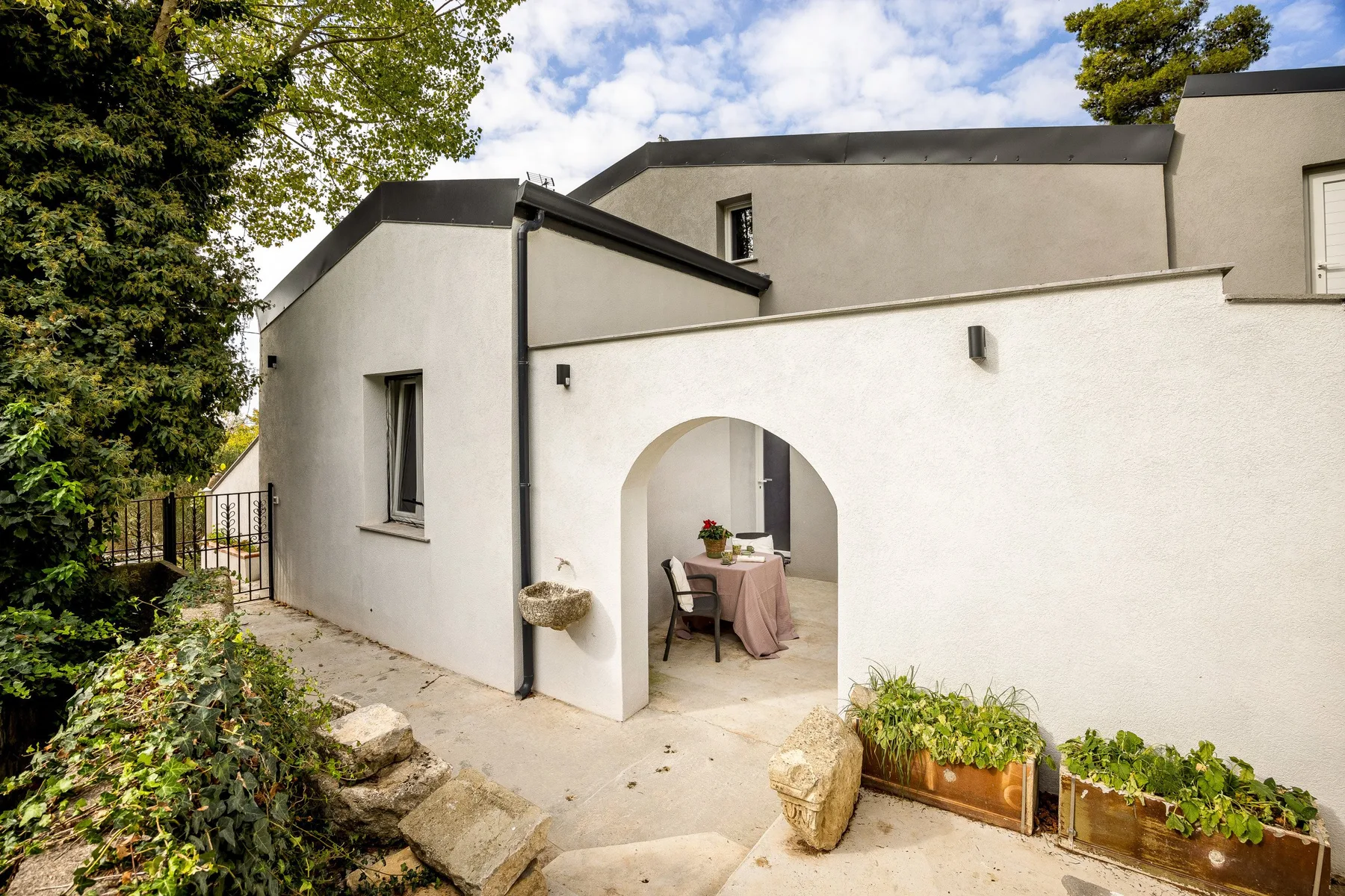 A white stucco house exterior with an arched opening and planters.