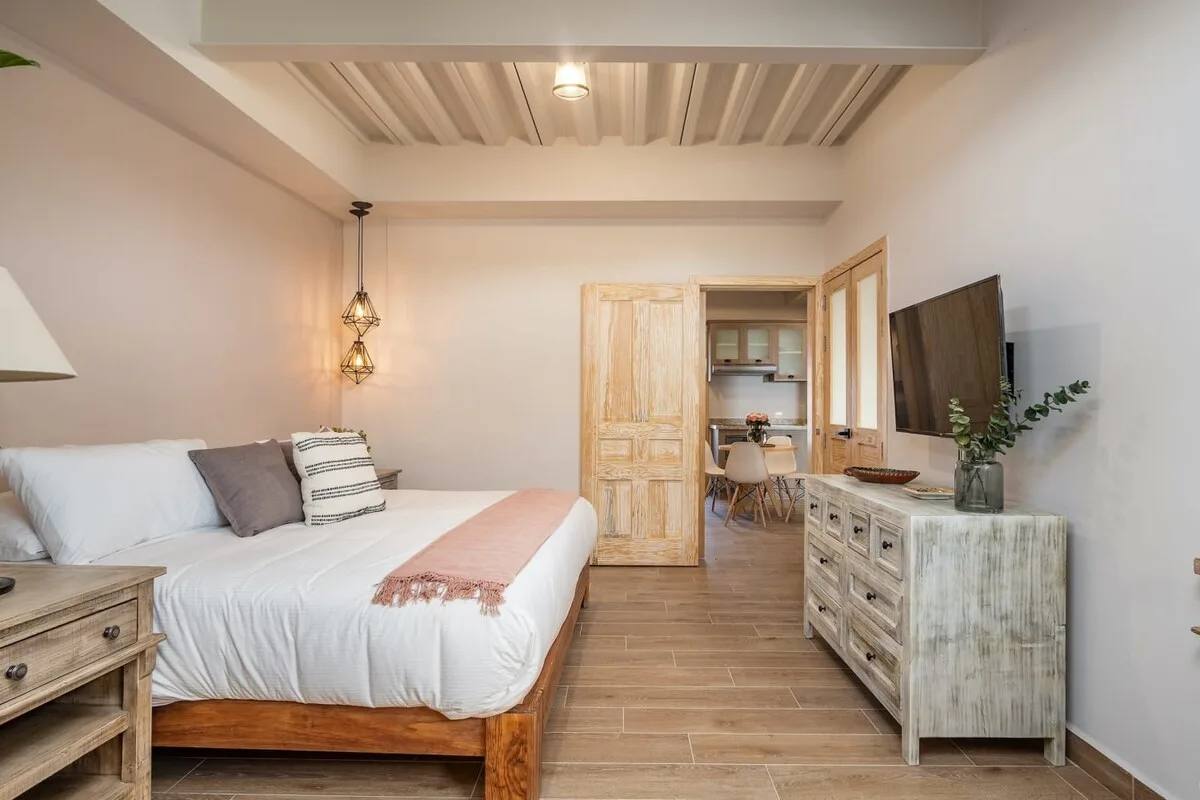 A bedroom with a bed, a wooden dresser, and an open doorway to a desk area.