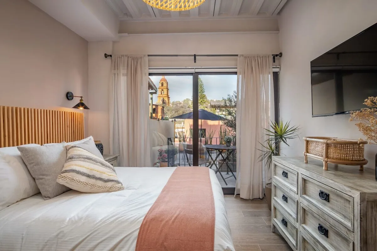 A bedroom with a bed, sliding glass doors, and a balcony beyond.