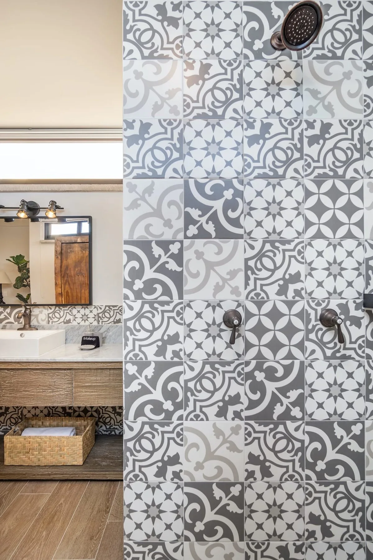 A bathroom vanity and mirror sit beside a shower wall with patterned tile.