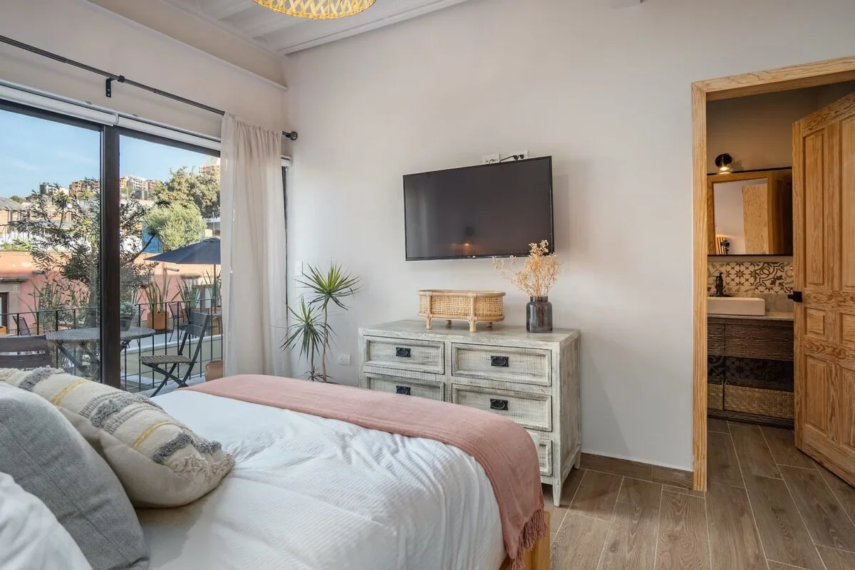 A bedroom with a bed, a wall-mounted television, and glass doors opening onto a balcony.