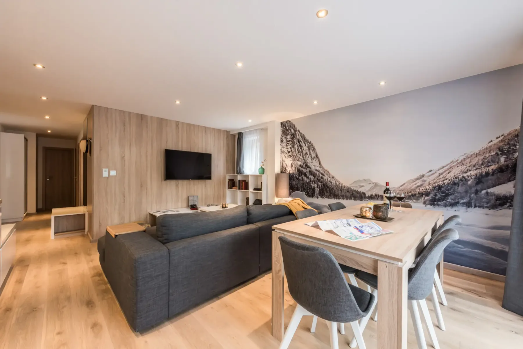 Una sala de estar y comedor moderna con asientos grises y un mural de montañas.