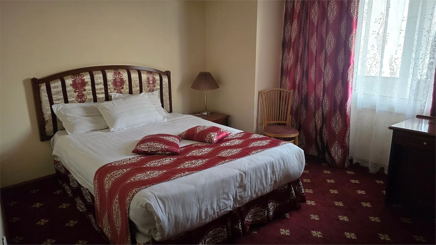 Espacio representativo del hotel: Dormitorio con una cama vestida con ropa de cama blanca y telas estampadas rojas.