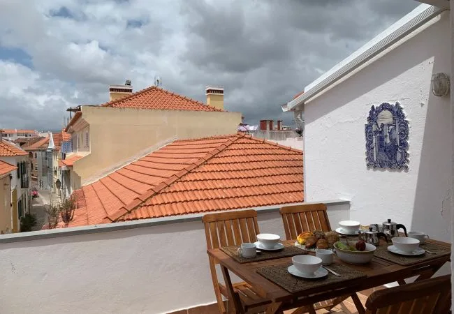 Una terraza en la azotea con una mesa de madera preparada para comer, frente a tejados de tejas.