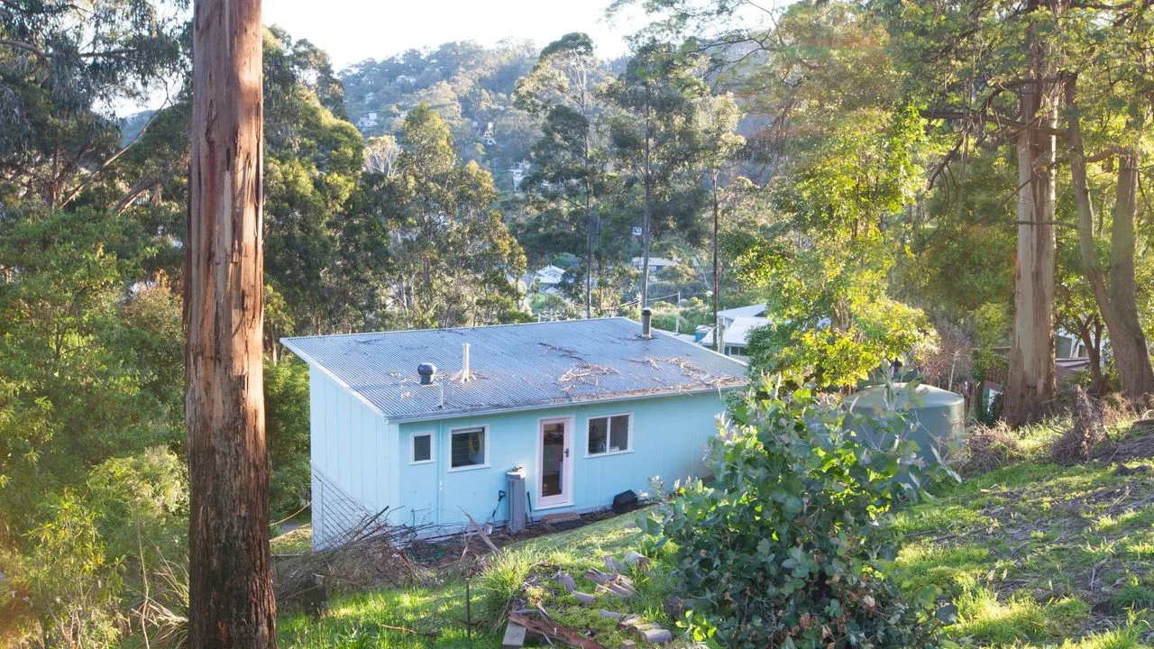 A small house sits among trees on a wooded hillside.