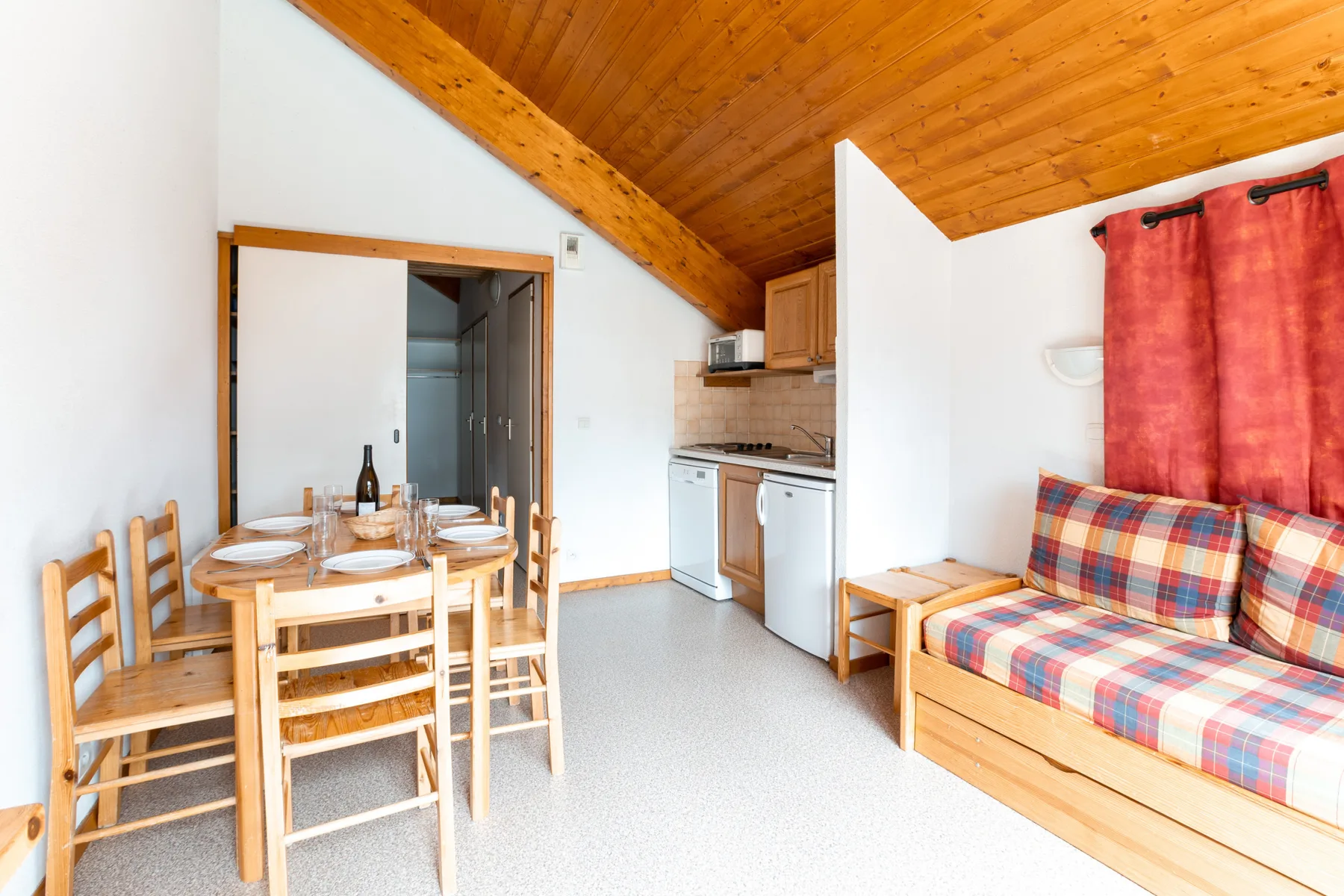 A compact living and dining area with a kitchenette and sloped wooden ceiling.