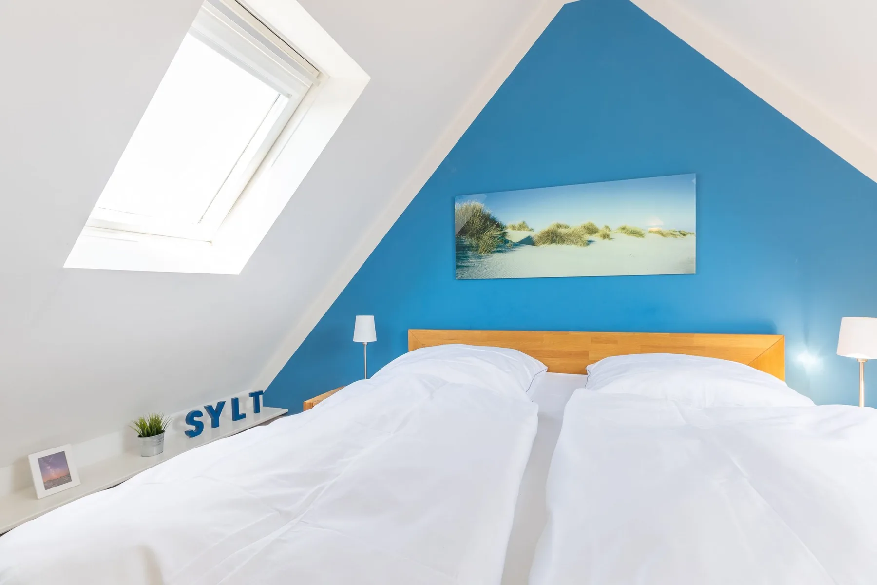 A bedroom with a bed beneath a sloped ceiling and a blue accent wall.