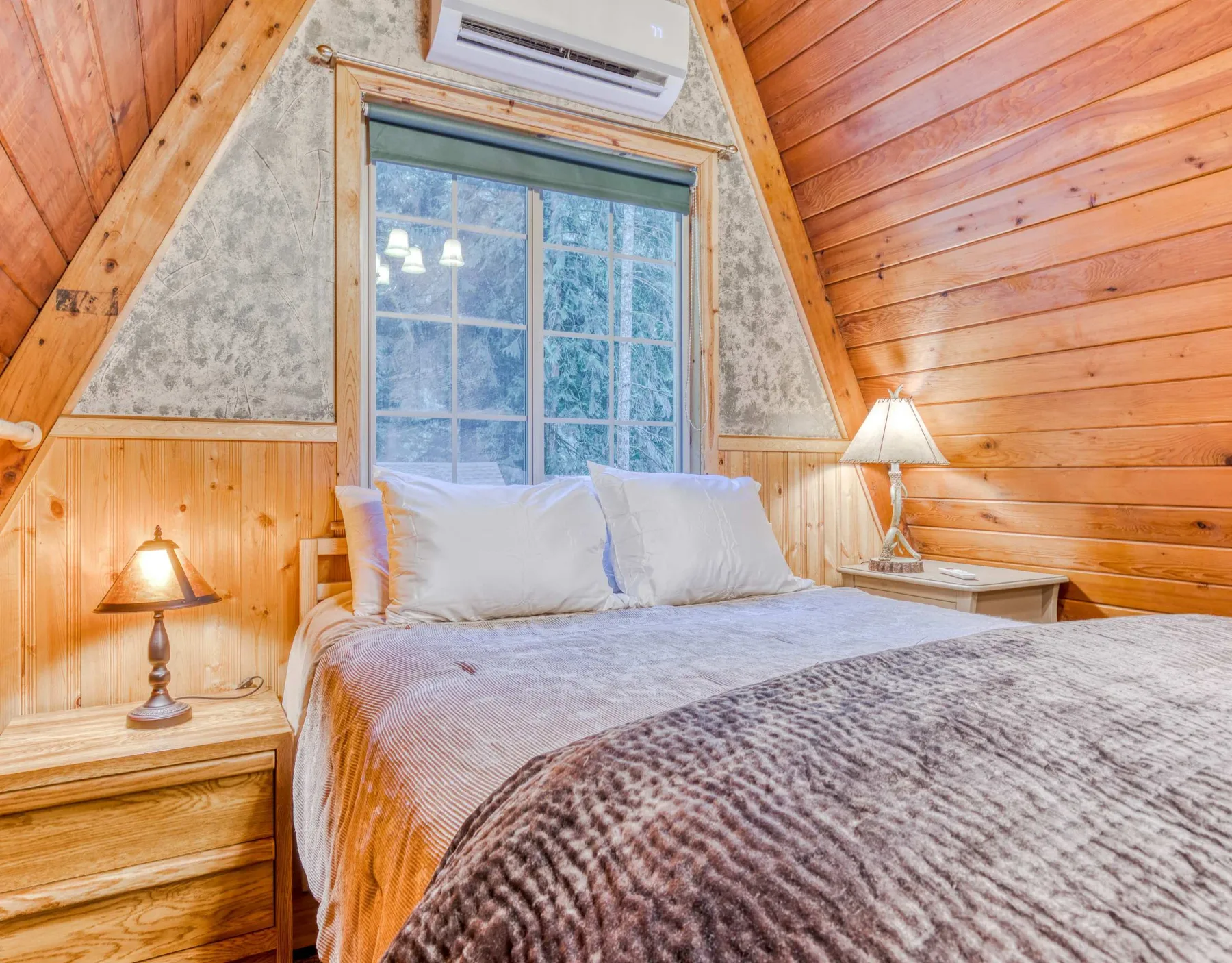 Un dormitorio con una cama bajo una ventana grande y paredes revestidas de madera.