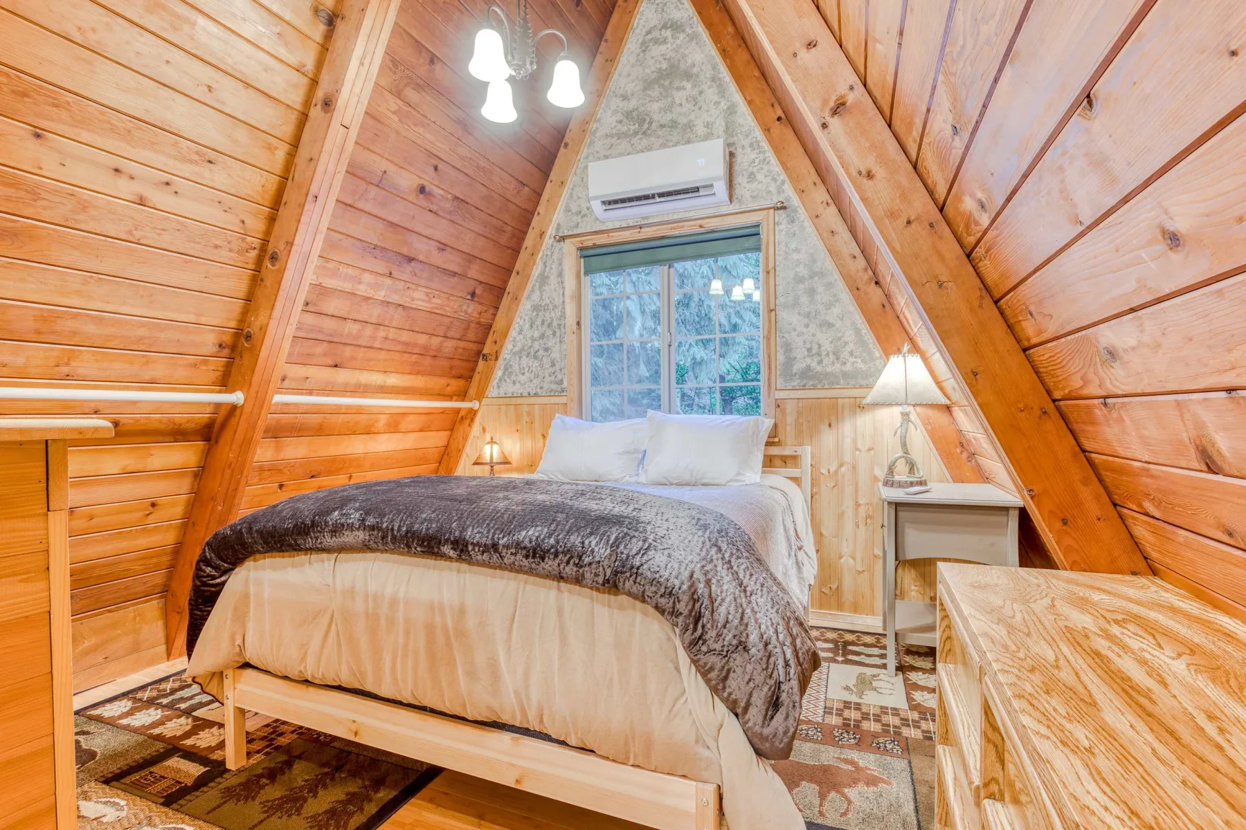 Dormitorio en forma de A con una cama bajo un techo inclinado de madera y una ventana.