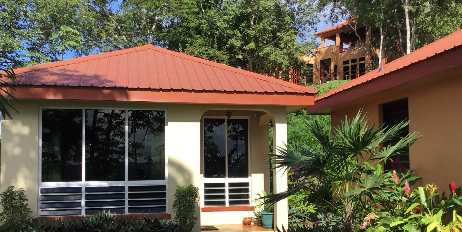 Representative hotel space: A low-rise building with a red roof sits among trees and tropical plants.