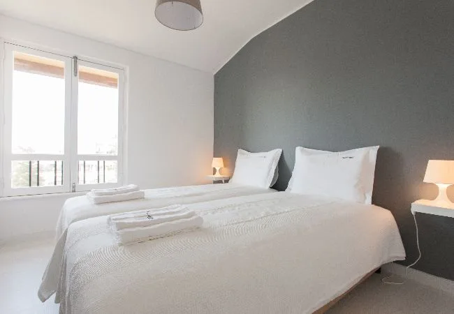 A bedroom with a neatly made bed and a large window.