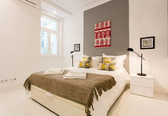 Un dormitorio luminoso con una cama bien arreglada y obras enmarcadas.