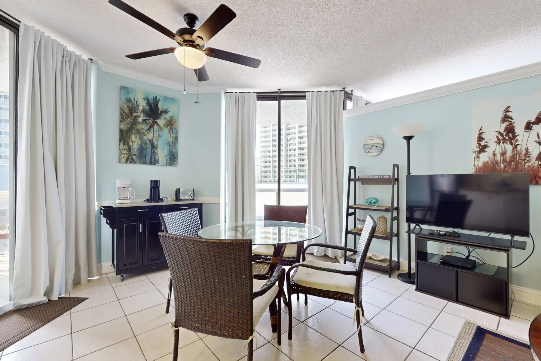 A bright dining and living area with a glass table and television.