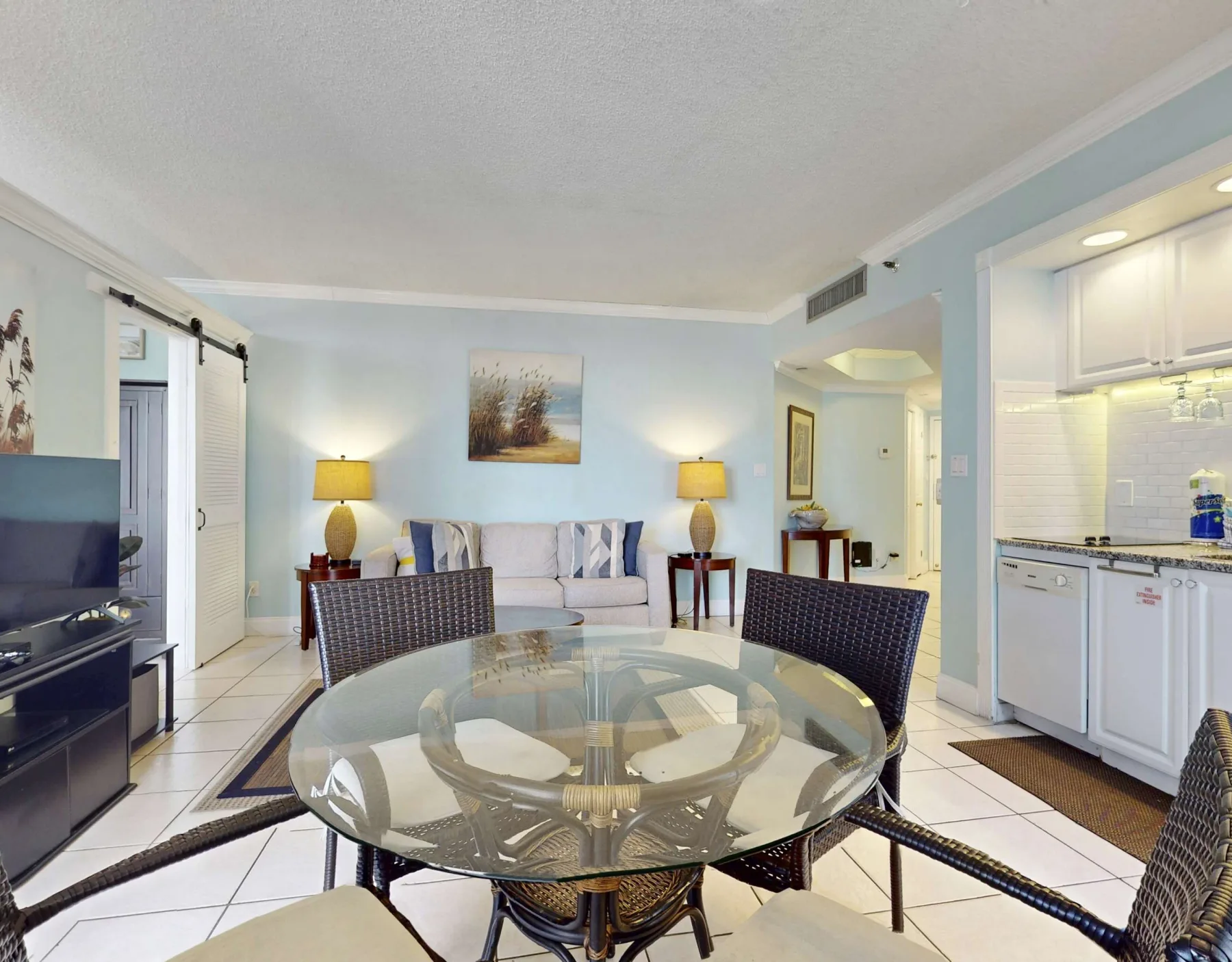 A living and dining area with a glass table, seating, and a compact kitchen.