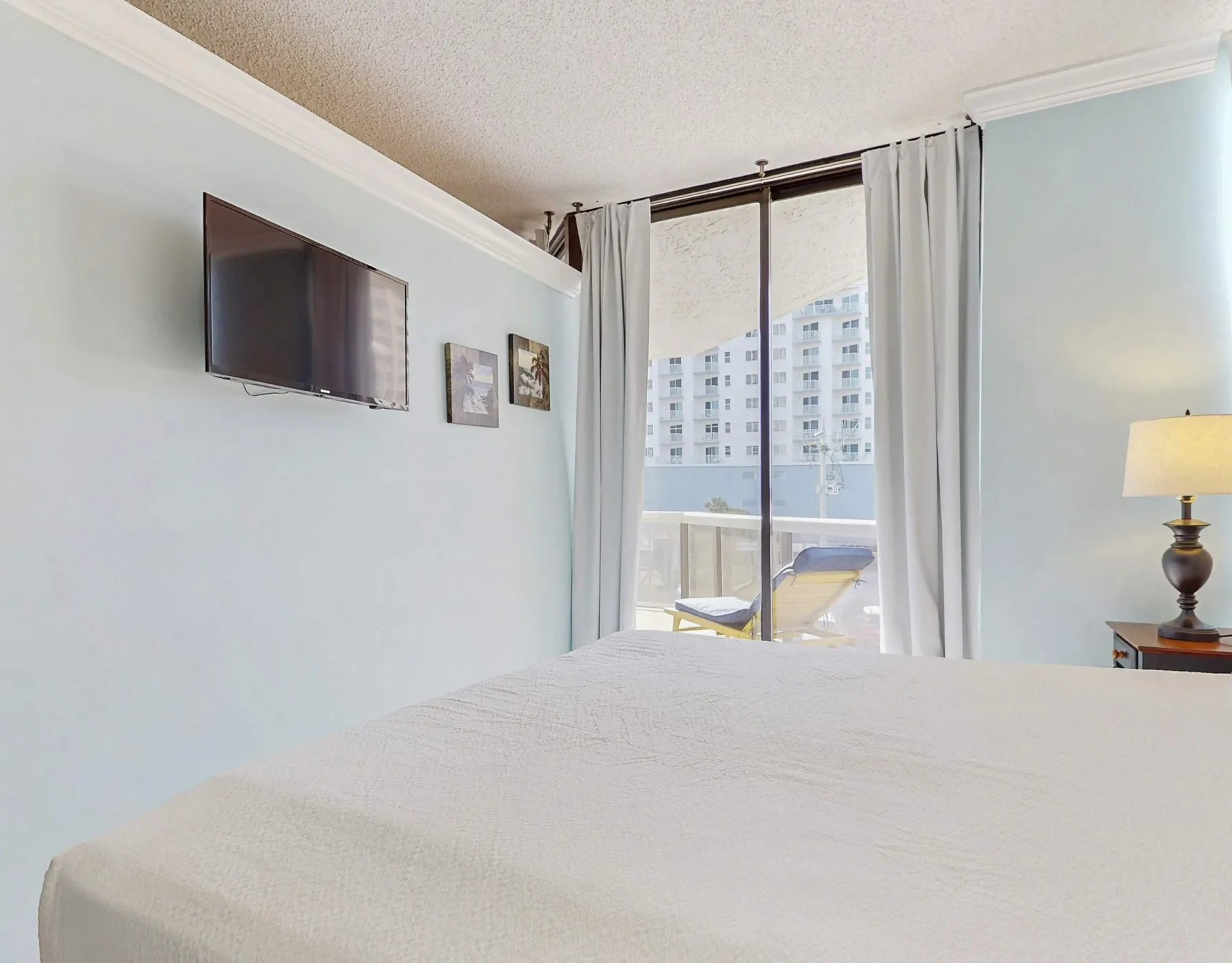 A bedroom with a bed, wall-mounted television, and curtained window.