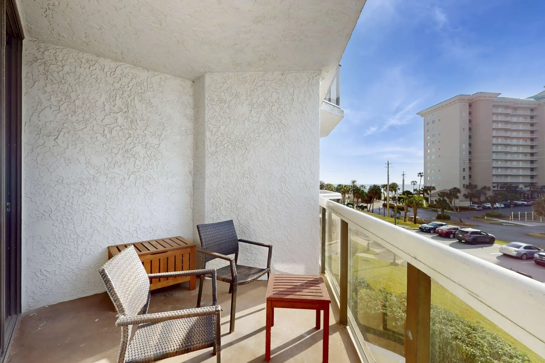 A balcony with seating and a glass railing overlooks a street and nearby buildings.