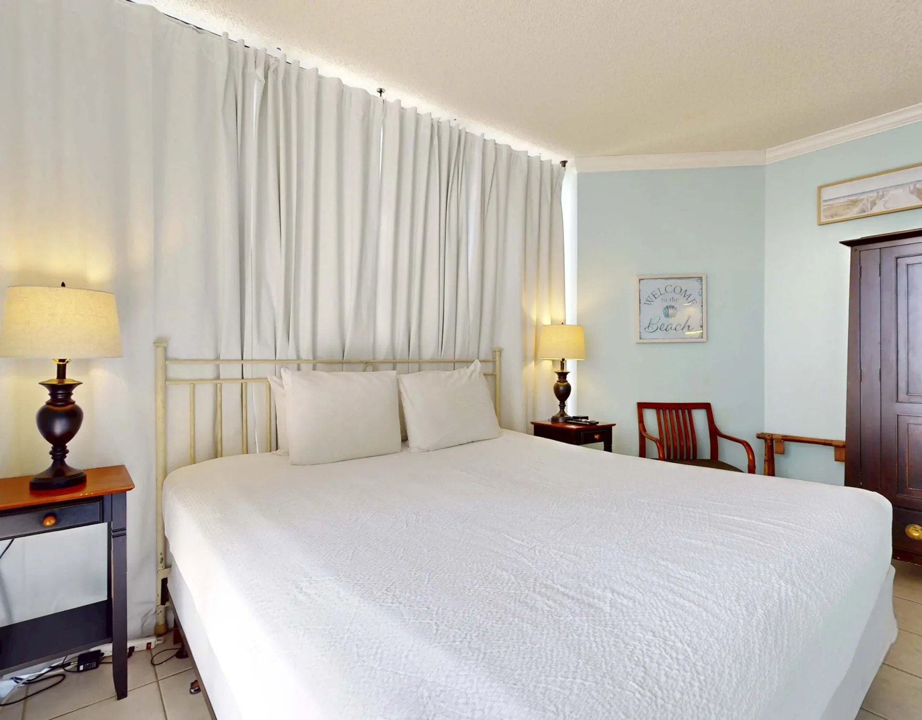 A bedroom with a large bed in front of white curtains.