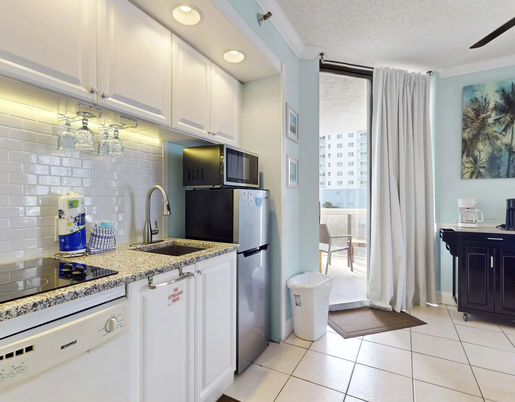 A bright kitchen with white cabinets and a sliding glass door opening to a balcony.