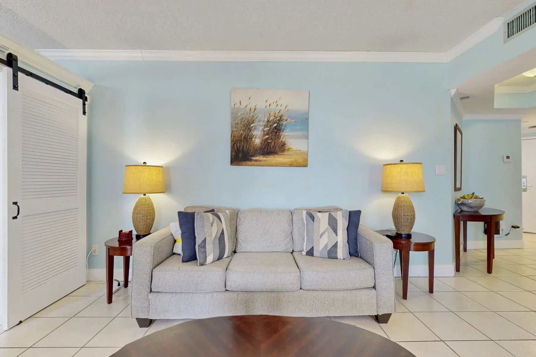 A living room with a sofa, matching table lamps, and artwork above.
