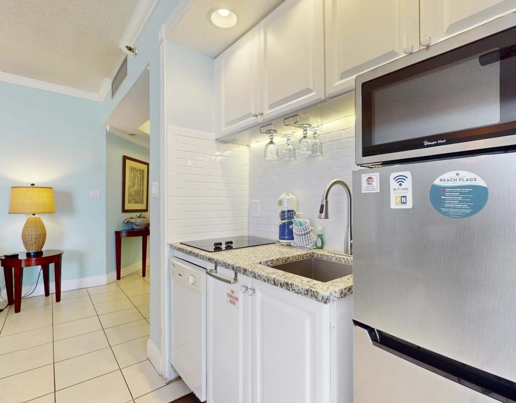 A compact kitchen with white cabinets, a sink, and a stainless steel refrigerator.