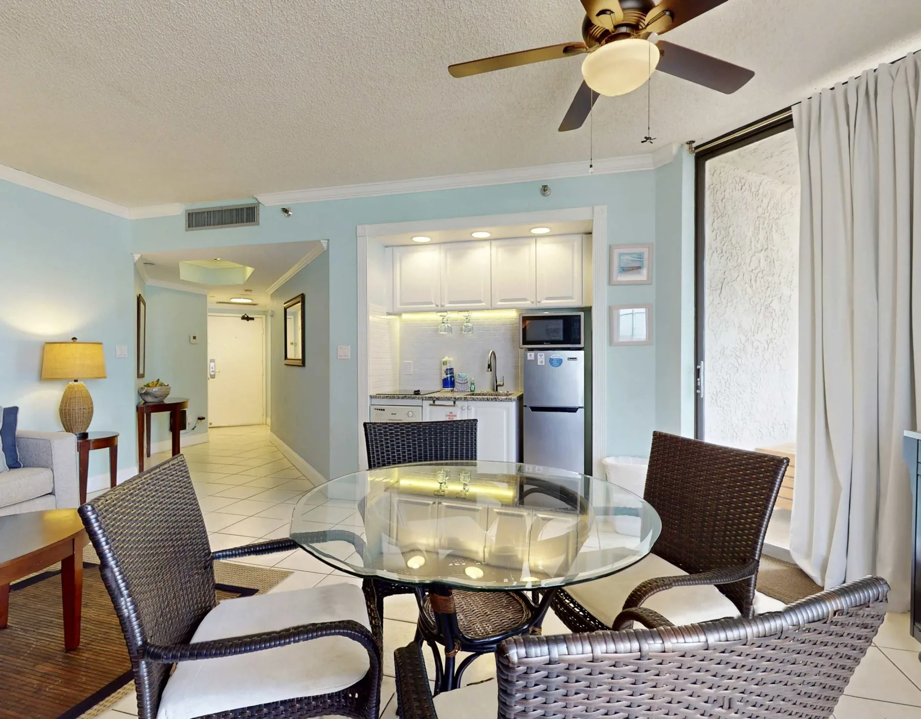 A dining area with a glass table and a compact kitchen in the background.