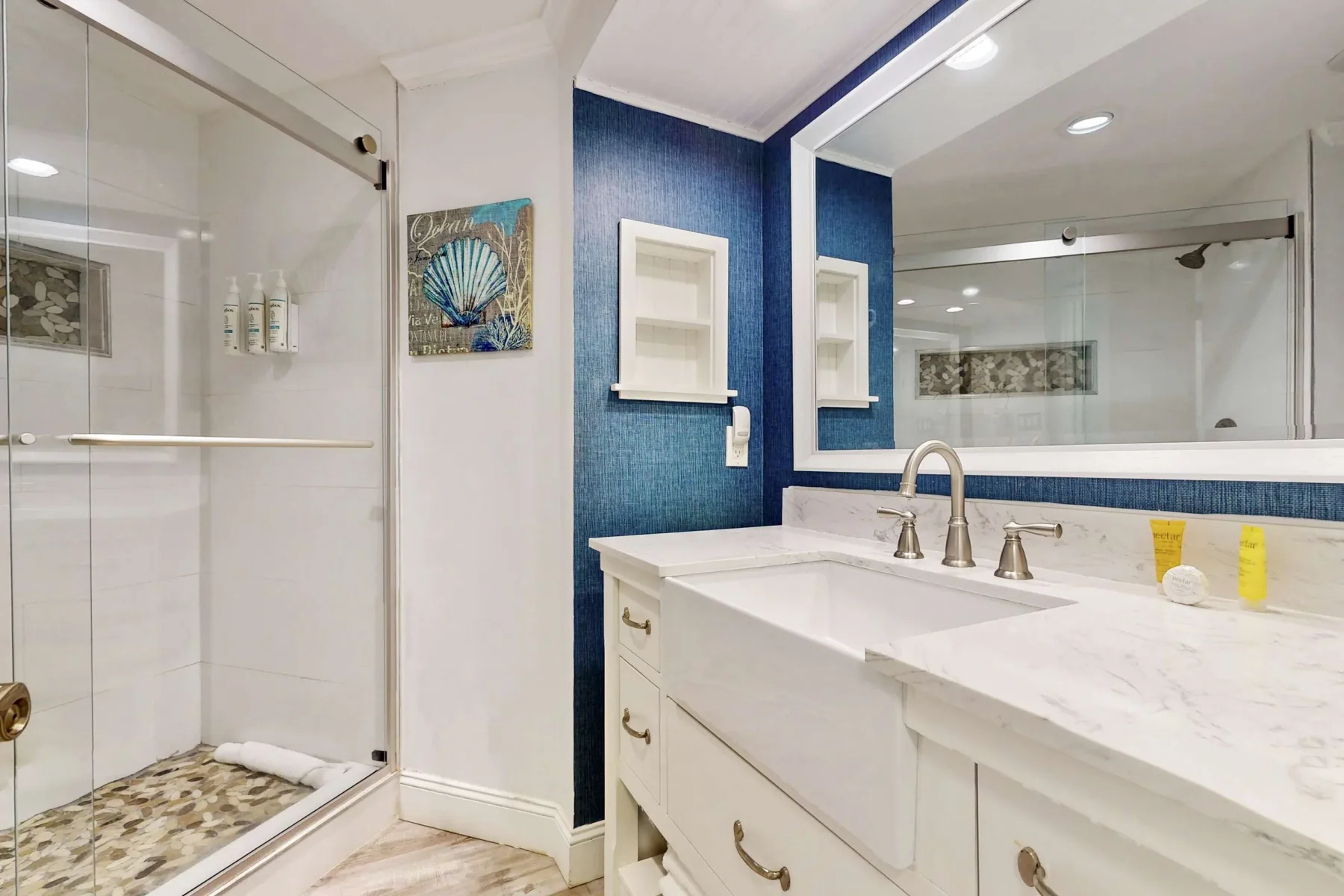 A bathroom with a glass shower, white vanity, and large mirror.