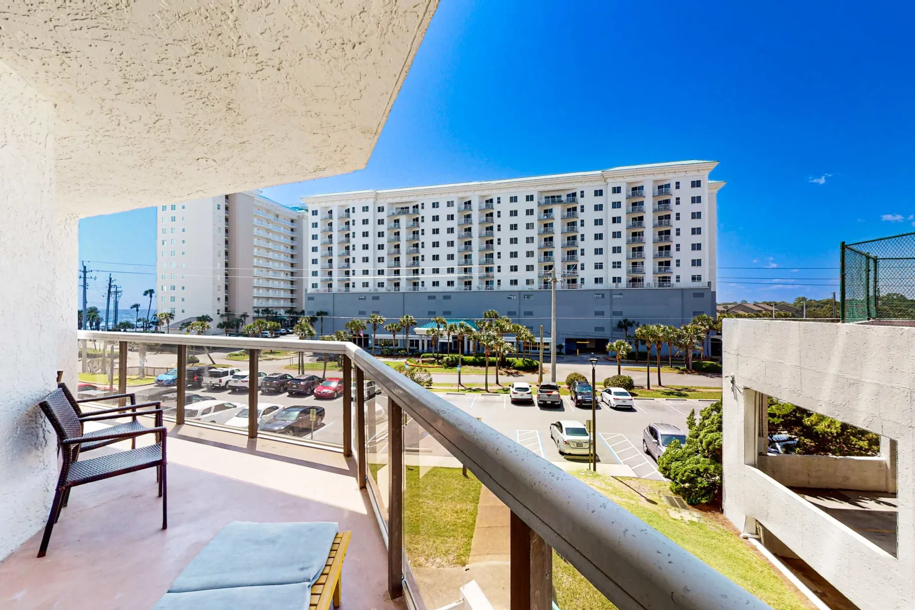 A balcony overlooks a parking area and a large multi-story building.