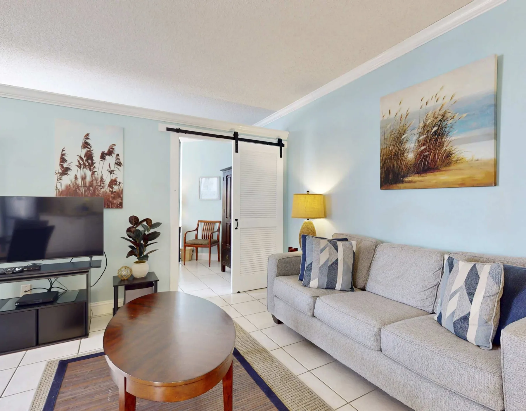 A living room with a light-colored sofa, television, and framed artwork.