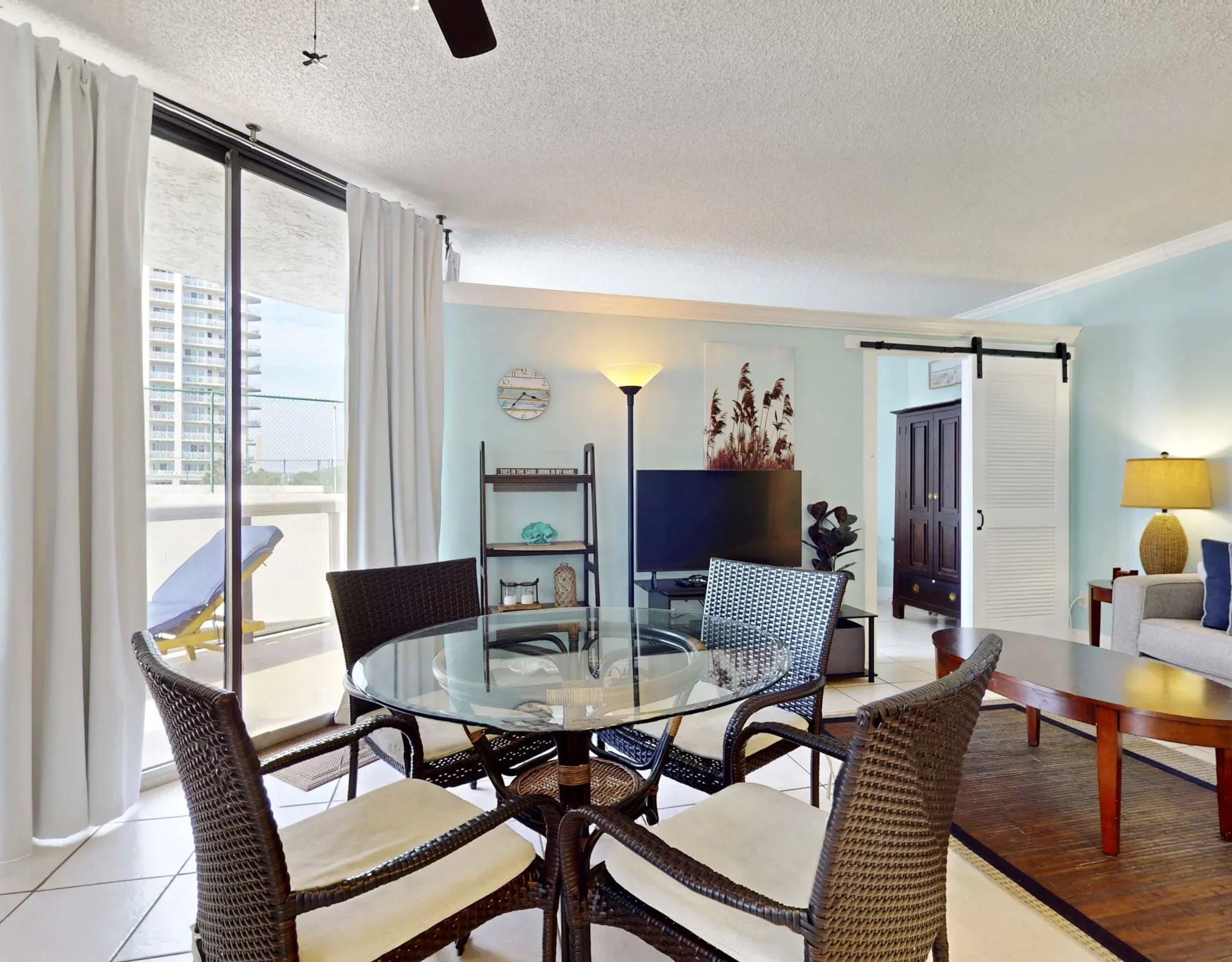 A living and dining area with a glass table, woven seating, and a television.