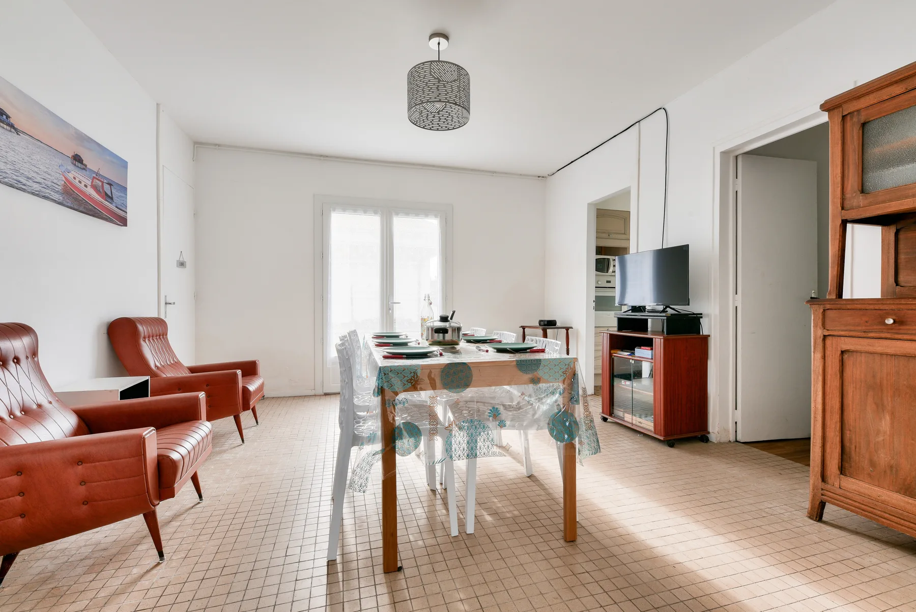 A bright dining and living room with a table, seating, and a television.
