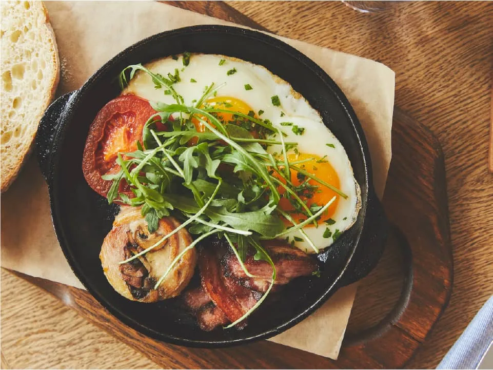 Espacio representativo del hotel: Un plato en sartén con huevos, hojas verdes y verduras asadas sobre una mesa de madera.