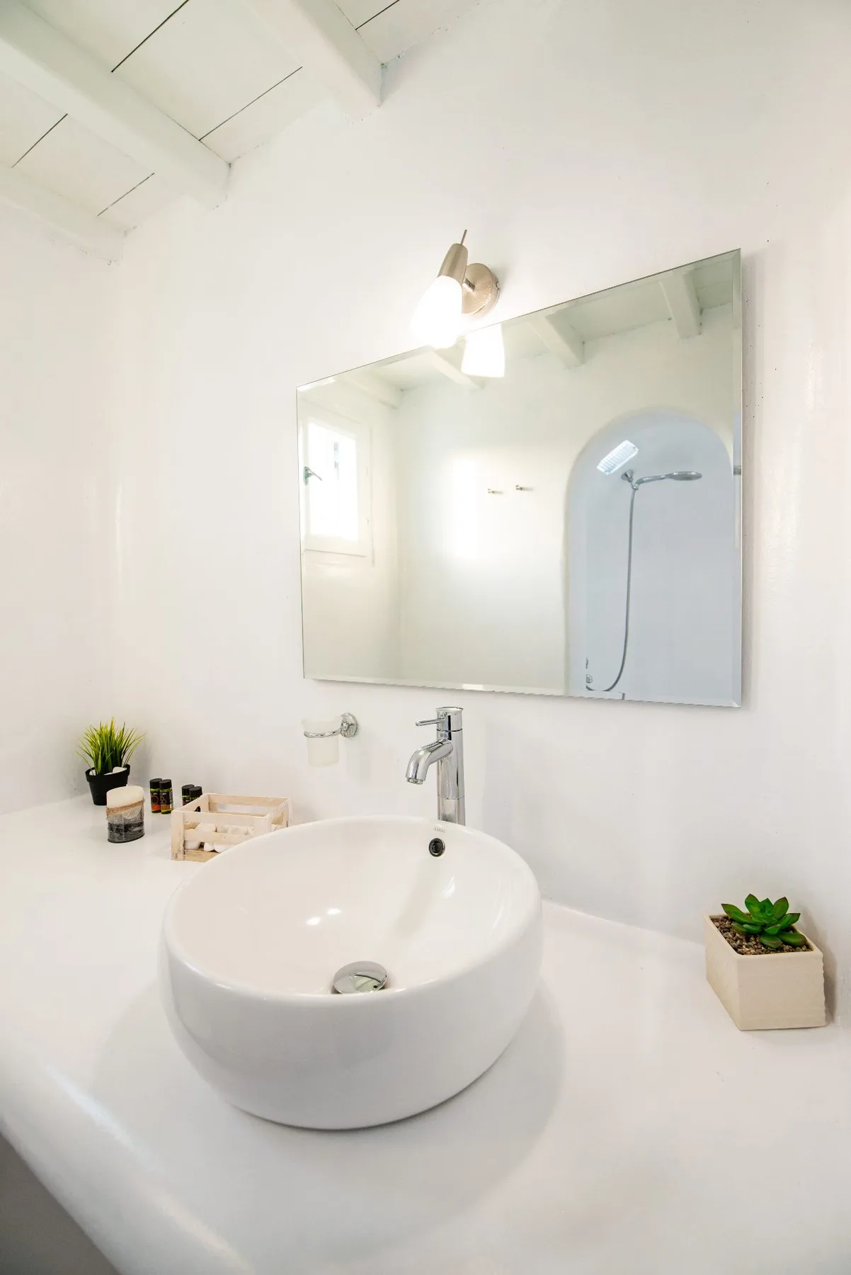 Un lavabo de baño luminoso con un lavamanos redondo, espejo y ducha visible en el reflejo.