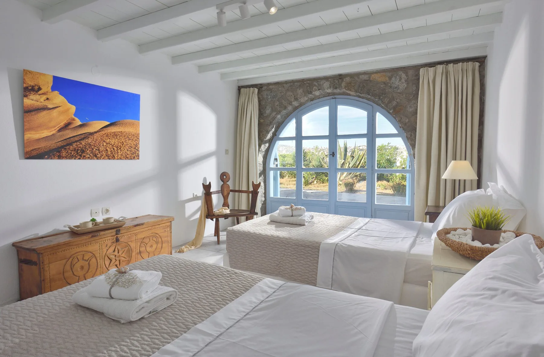 Un dormitorio luminoso con dos camas y una gran ventana arqueada.