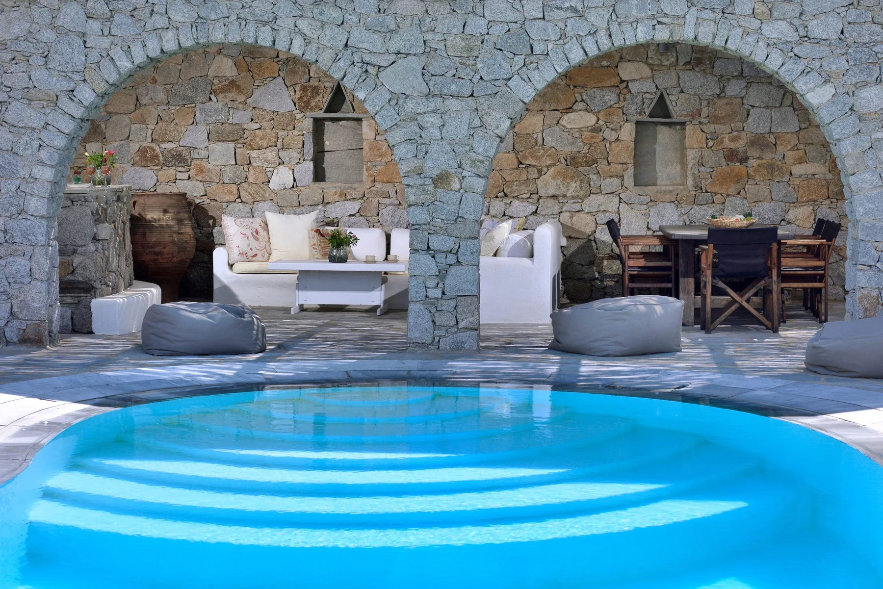 Una piscina está frente a un patio de piedra con asientos bajo arcos.