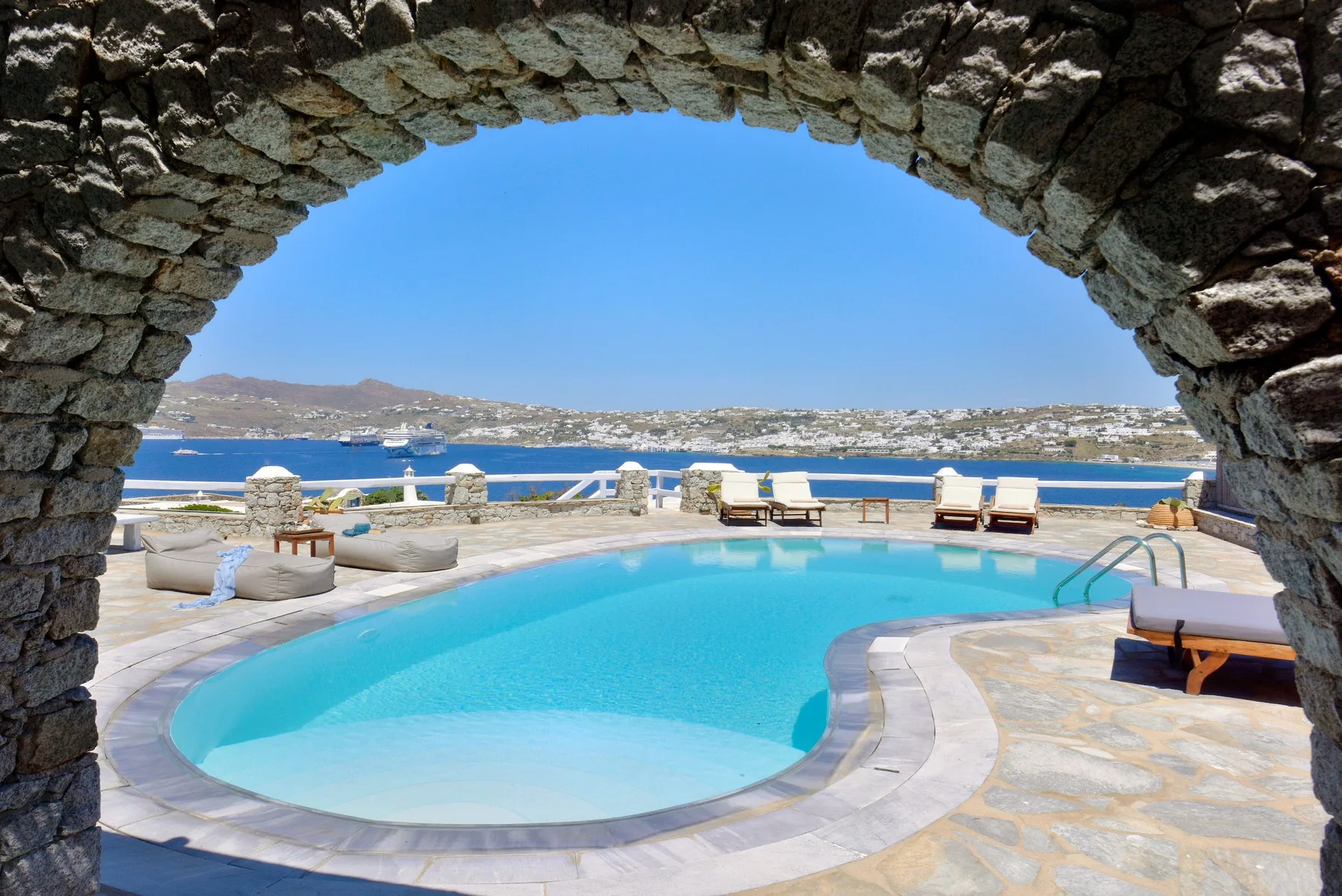 Una piscina curva está junto al mar bajo un arco de piedra.