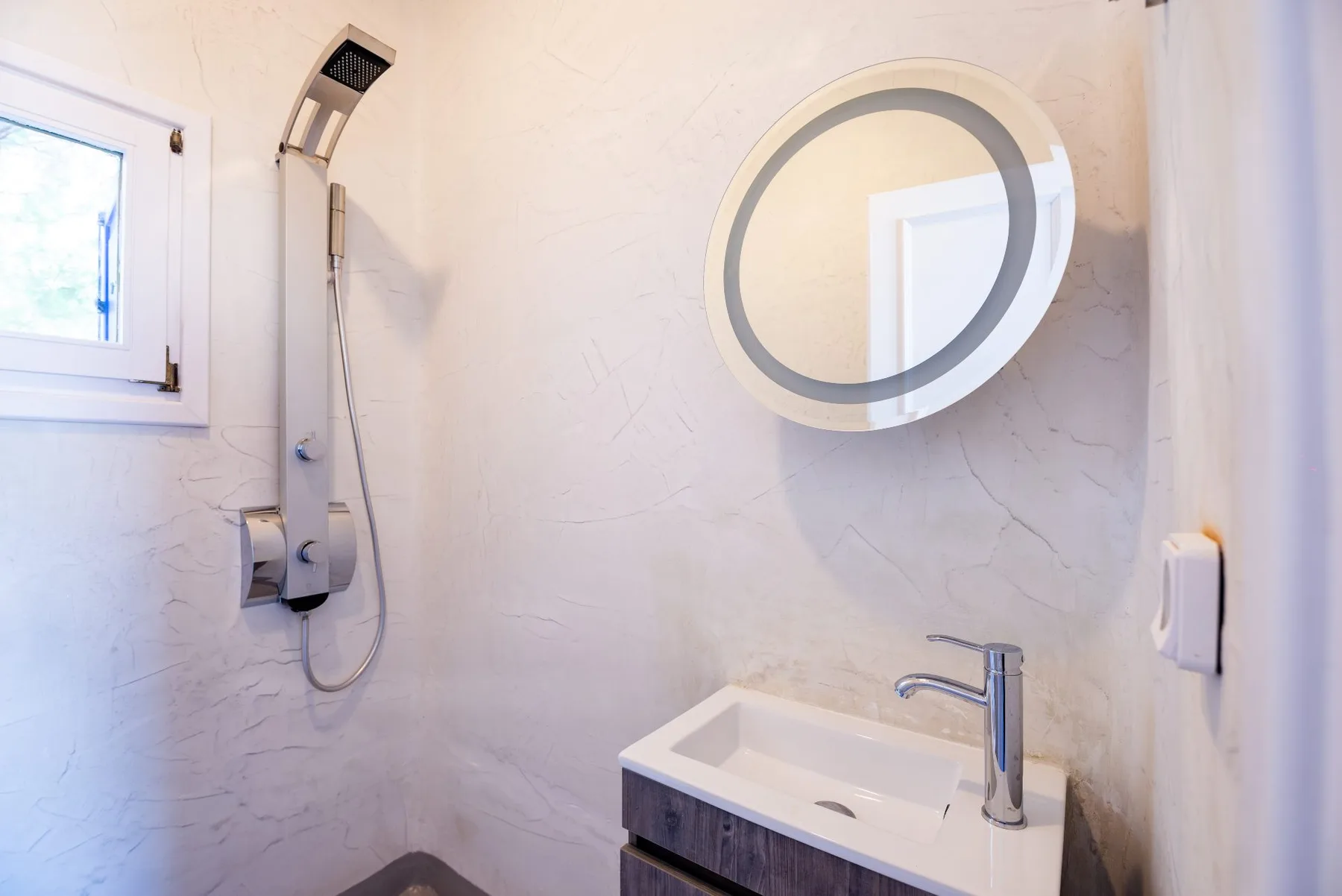 Un baño luminoso con ducha de pared, espejo redondo y lavabo.