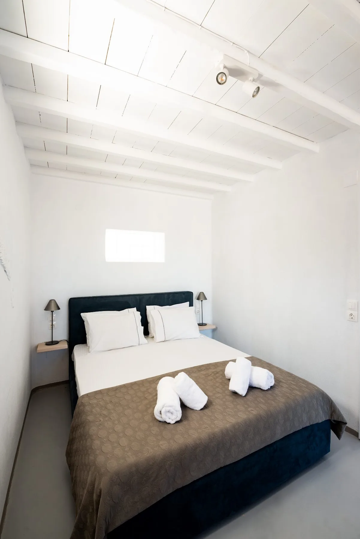 Un dormitorio con una cama bien tendida y vigas blancas en el techo.