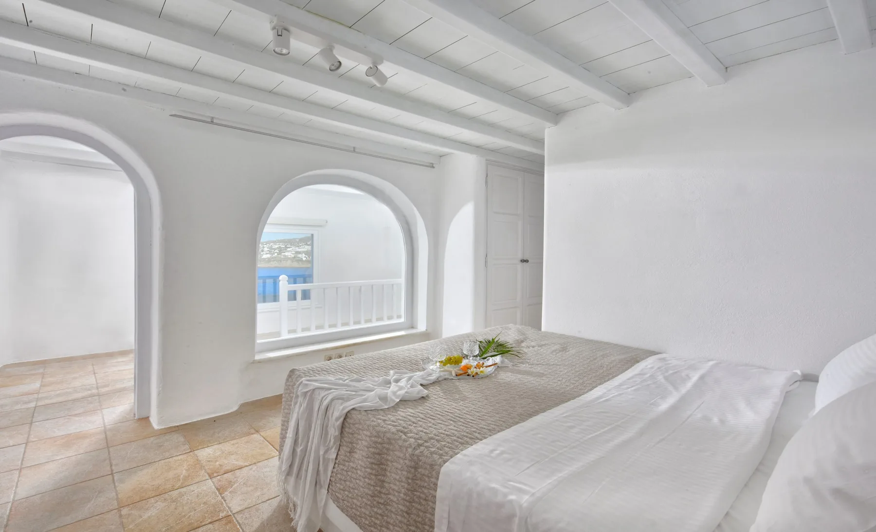 Un dormitorio luminoso con una cama junto a arcos que dan al agua.