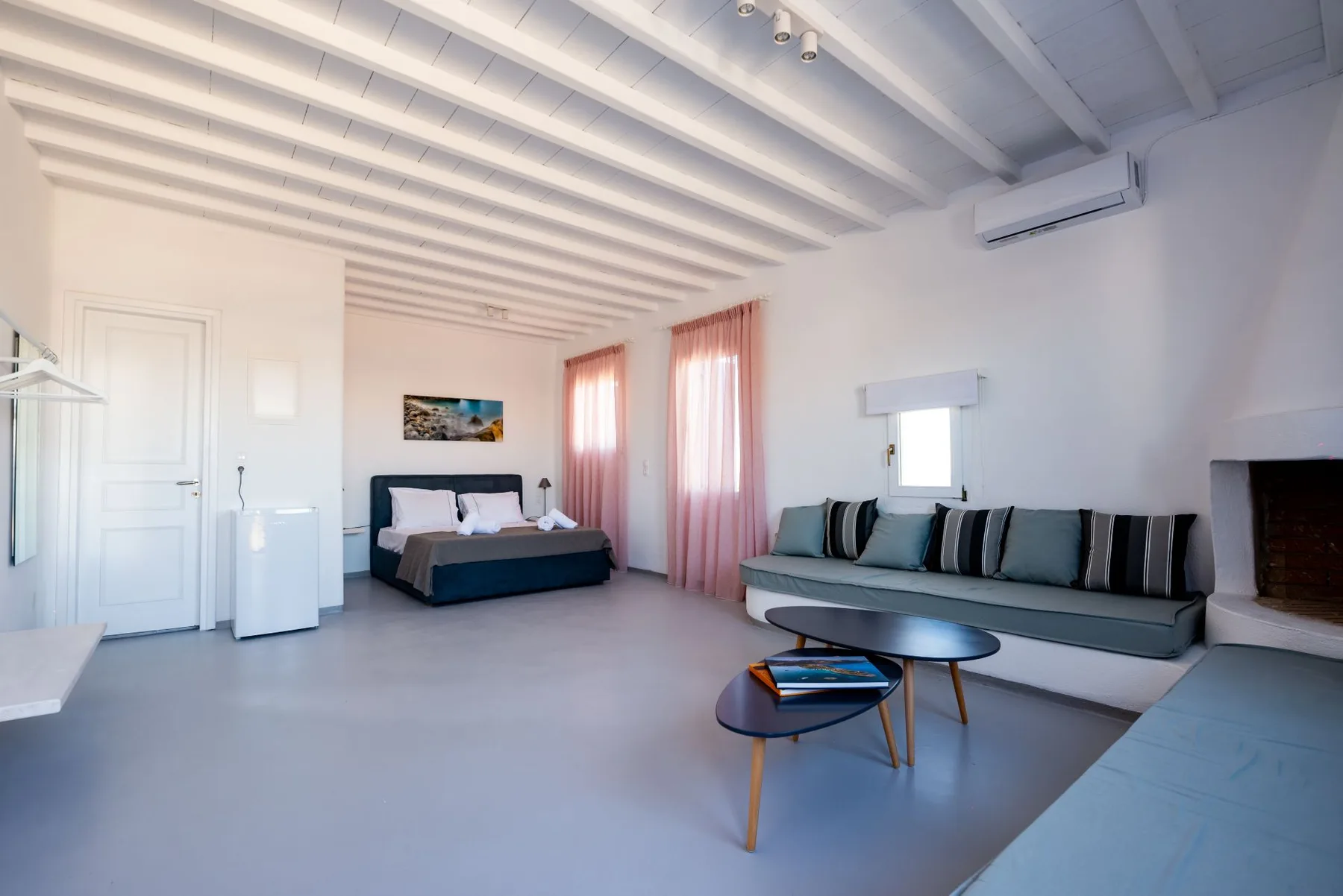 Una luminosa sala de estar y dormitorio con cama, asientos y cortinas rosas.