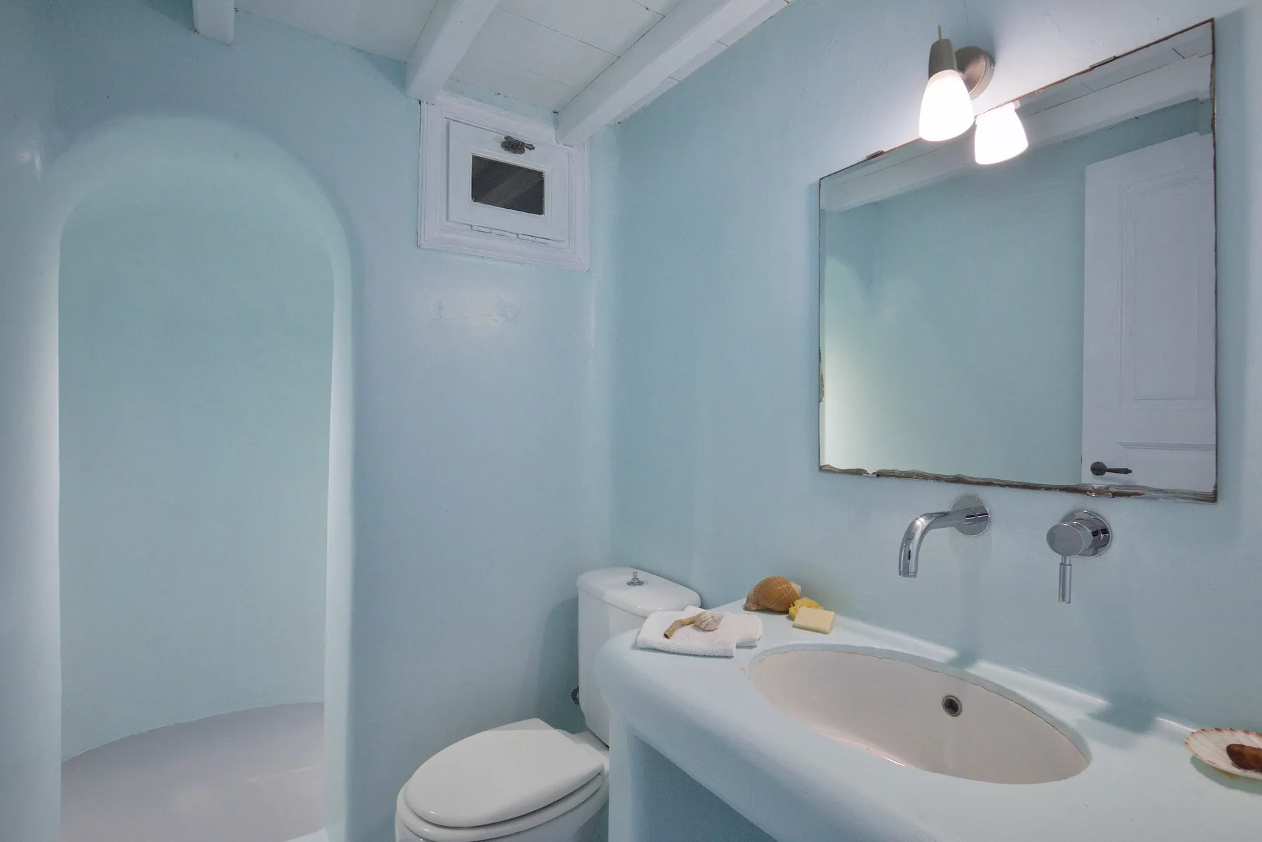 Un baño azul claro con lavabo, espejo e inodoro.