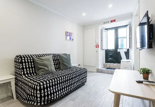 A bright living room with patterned seating, a wall-mounted television, and a table.