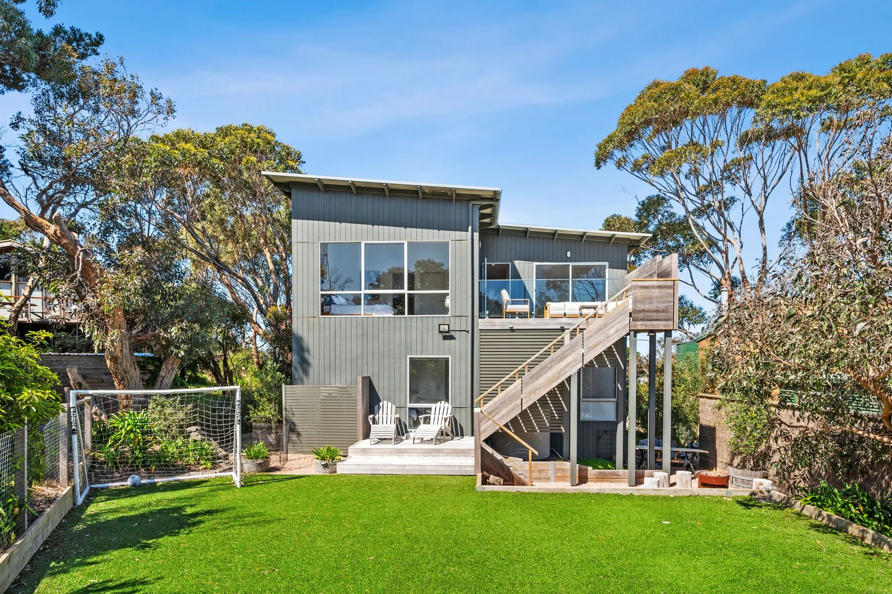 A modern house overlooks a green lawn, with an elevated wooden deck and stairs.