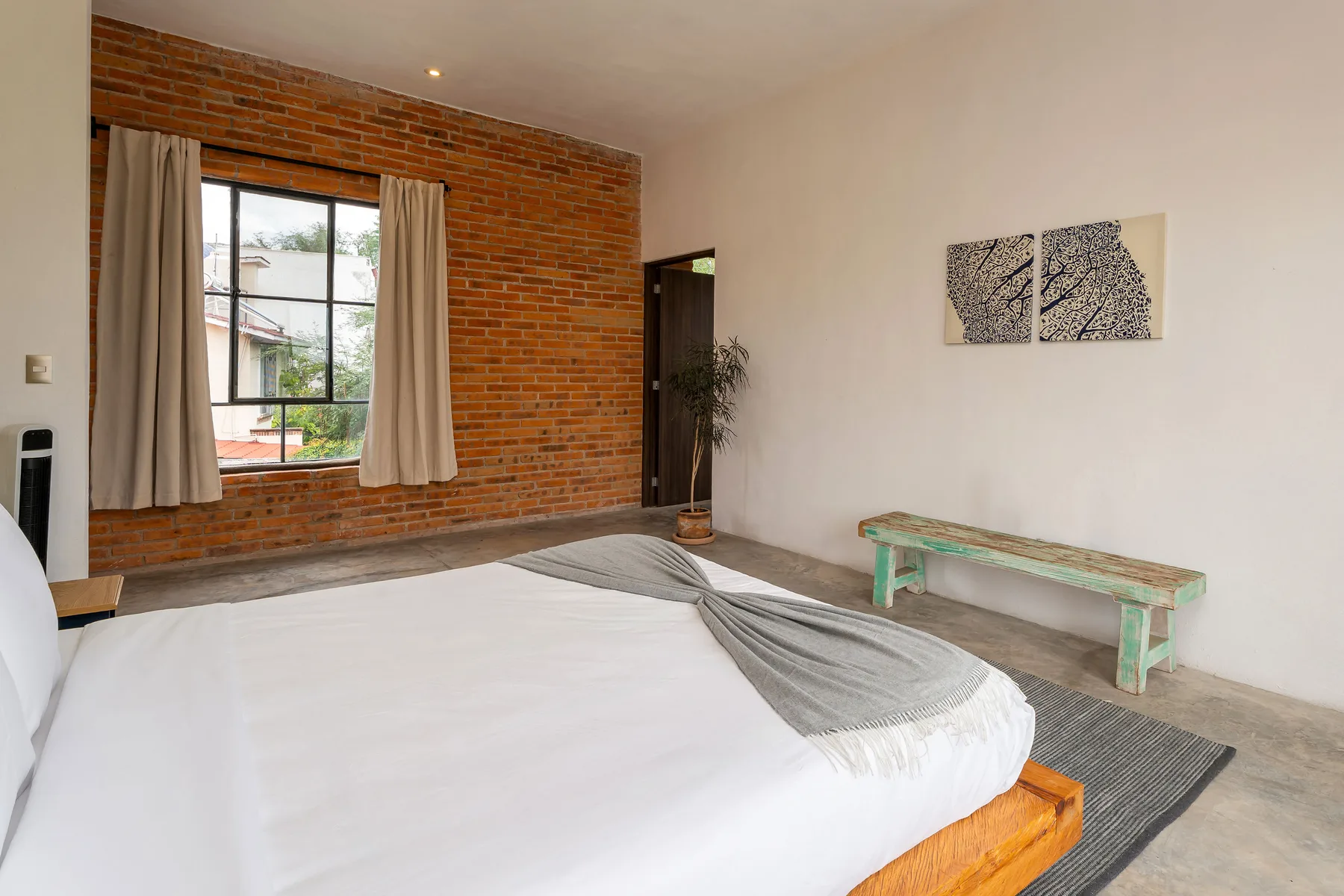 A bedroom with a brick accent wall, curtained window, and bed.