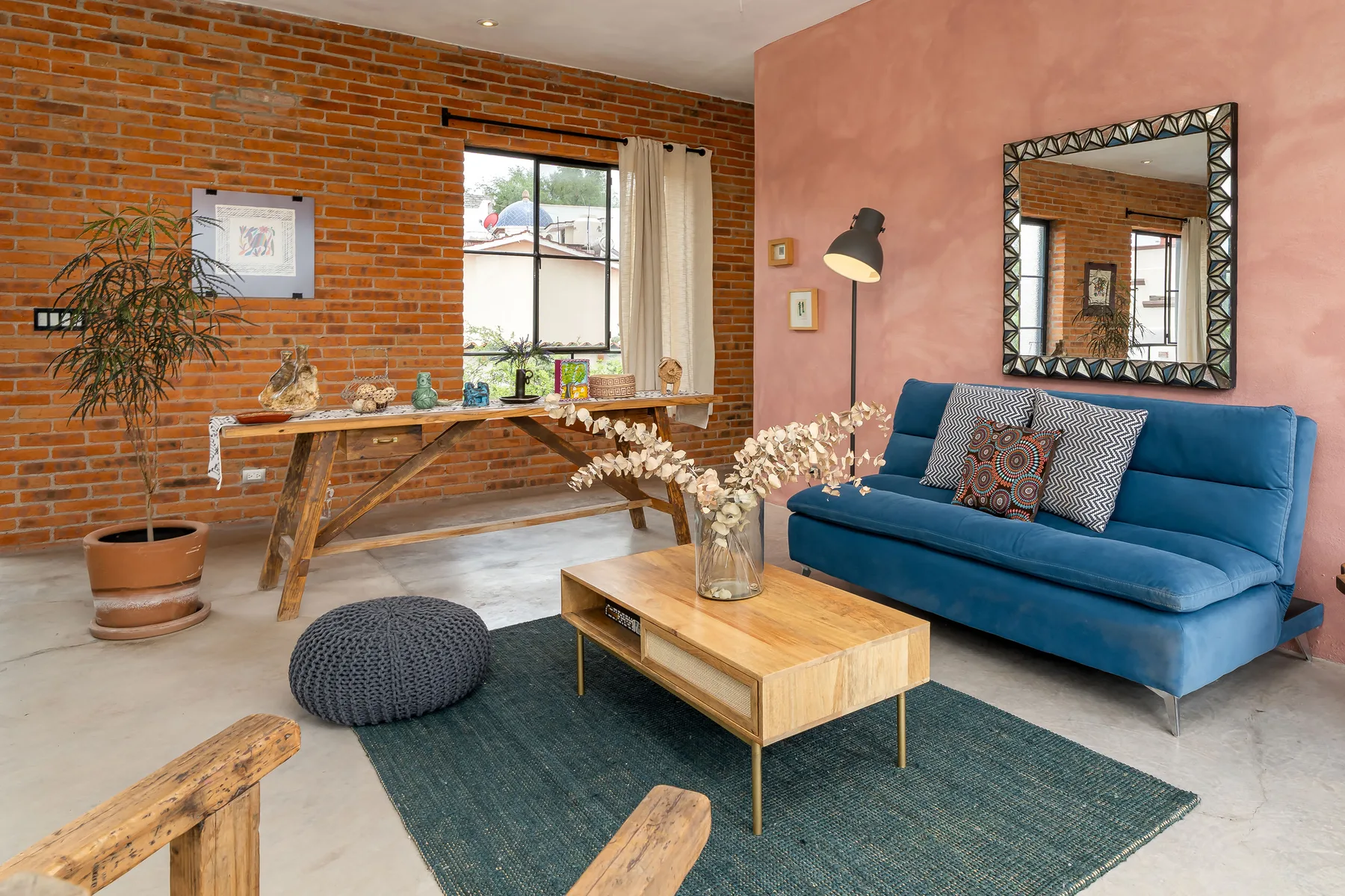 A living room with blue seating, a wooden coffee table, and exposed brick walls.