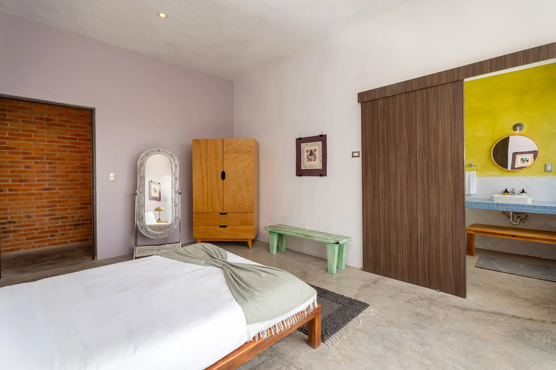 A bedroom with a bed, wooden wardrobe, and an open doorway to a washroom.