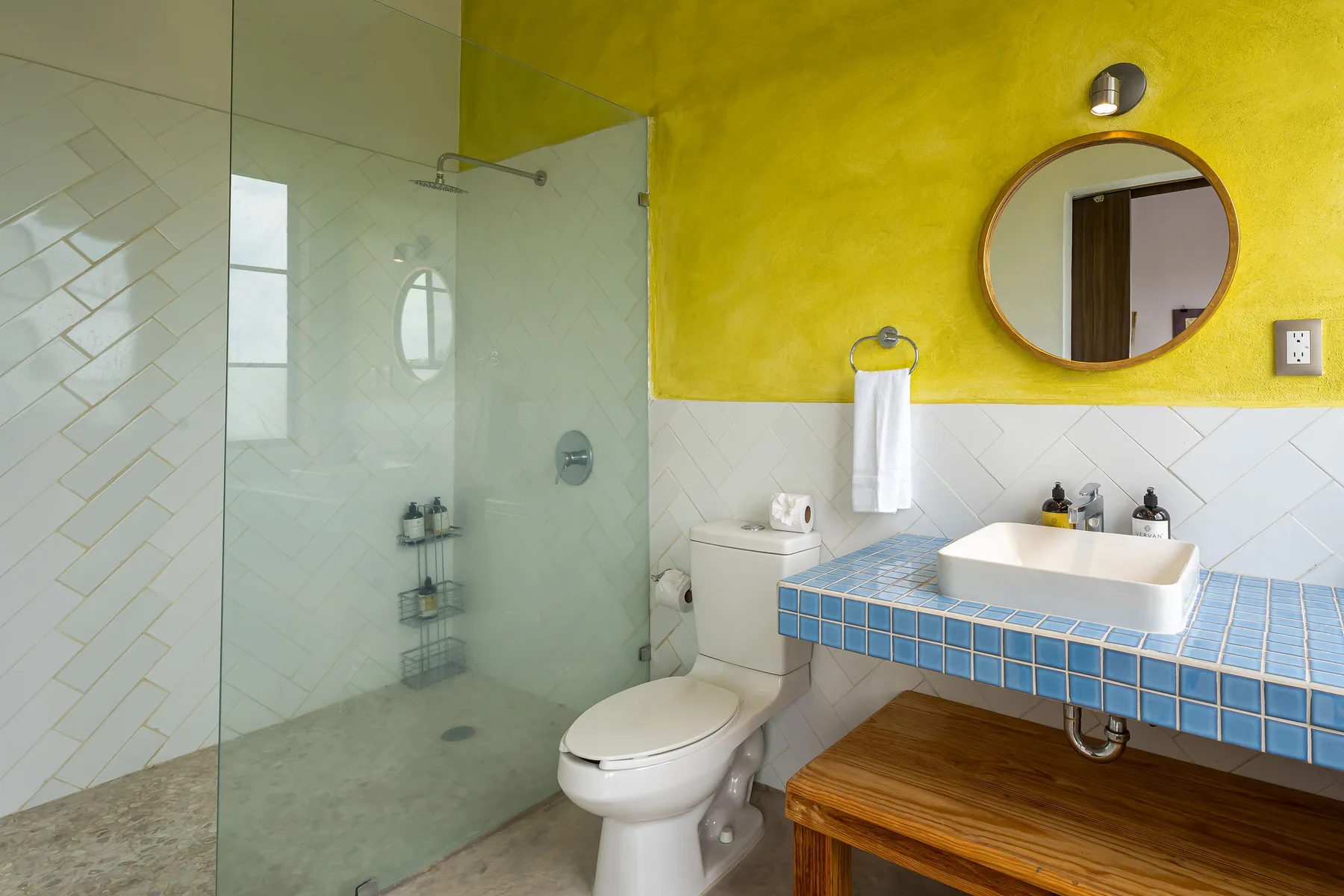 A bathroom with a glass shower, toilet, and blue-tiled vanity.