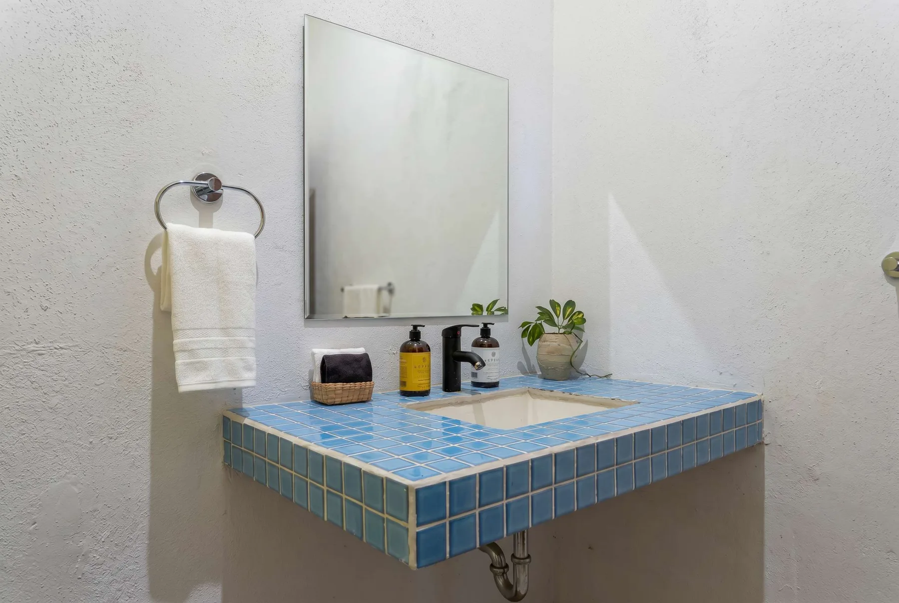 A bathroom vanity with a blue tiled counter, sink, and wall mirror.