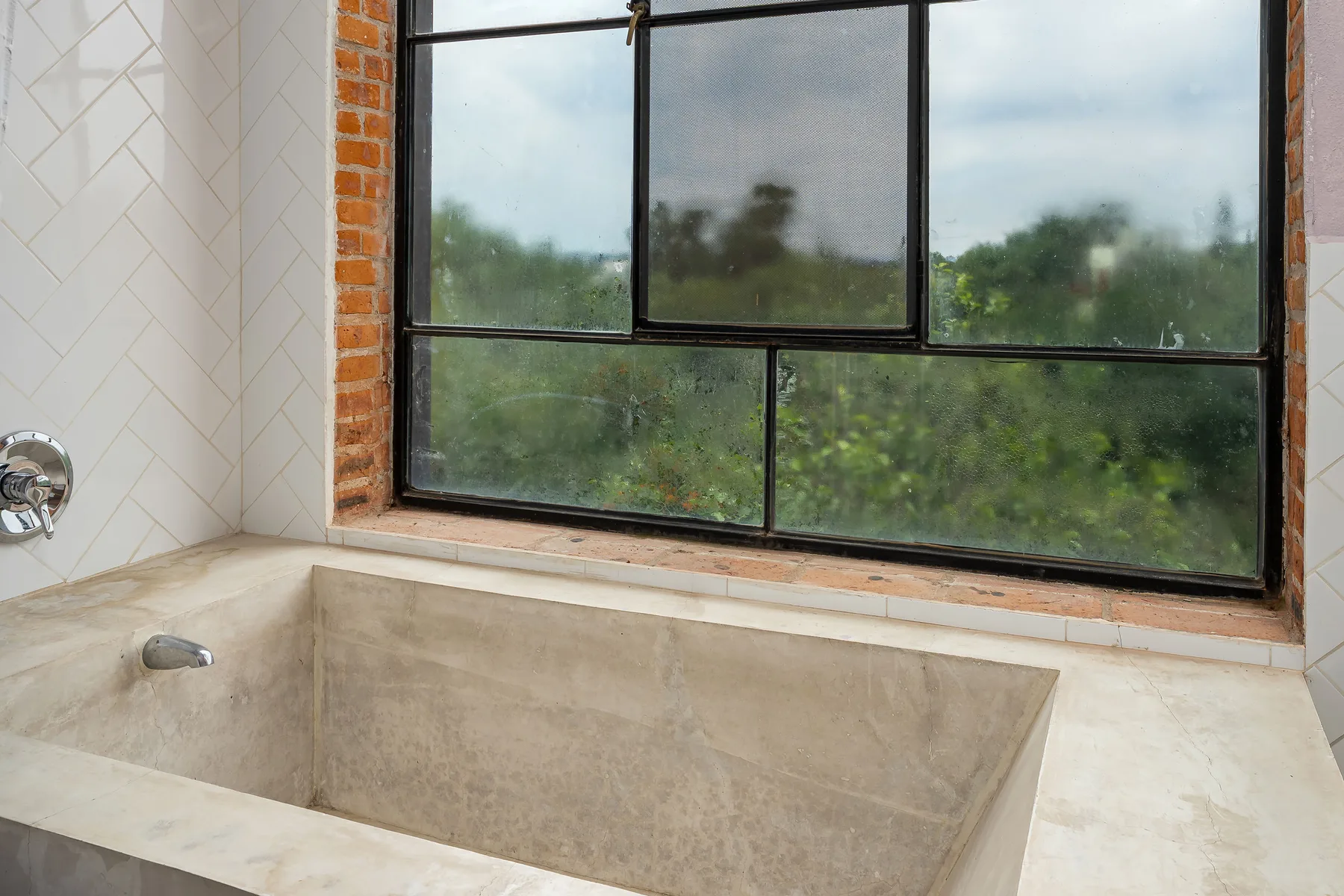 A built-in bathtub sits beneath a large window.