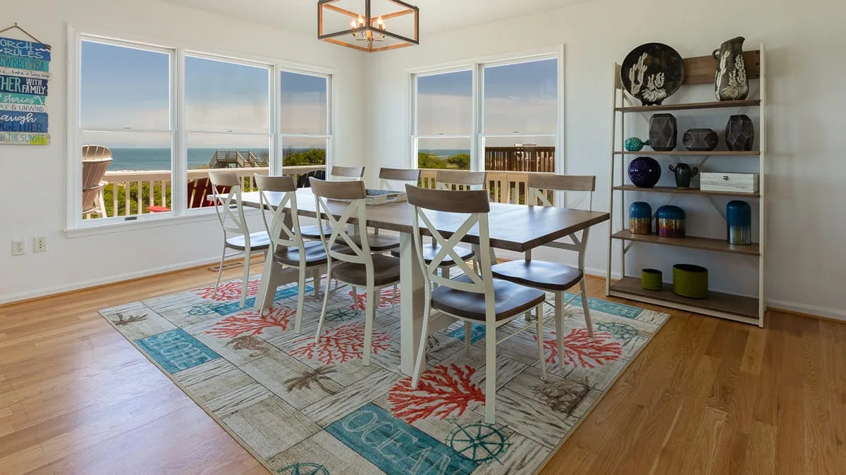 A bright dining area with a long table and seating beside large windows.